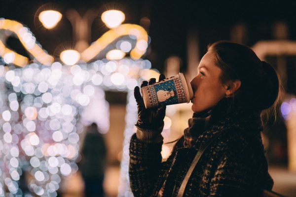 women drinking coffee with Christmas lights behind her